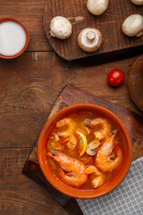 Tom yam soup with shrimps in a plate on a wooden table on a napkin next to a bowl with coconut milk mushrooms and tomatoes.