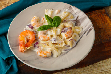 Farfalle pasta with shrimps in a creamy sauce on a gray plate on a wooden table on a blue napkin.