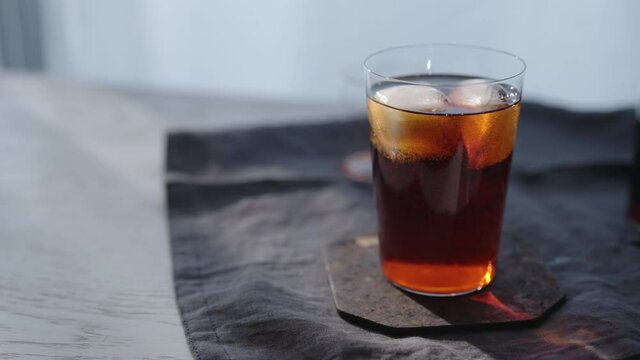 Tracking shot of cocktail aperetivo in tumbler glass with window on background