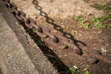 Metal links of a chain, rusty links of a large chain, a fragment of a fence on the background of the earth