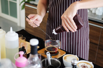 Asian barista young man is smiling and pouring fresh chocolate in glass cup for make coffee. Start up for cafe business concept.