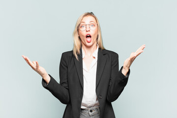 young pretty businesswoman feeling extremely shocked and surprised, anxious and panicking, with a...