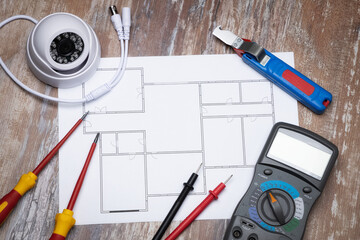 A set of electrical instruments laying on blueprint. Multimeter, screwdrivers and security camera.