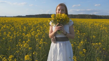 A girl in a white dress is walking among a rapeseed field.