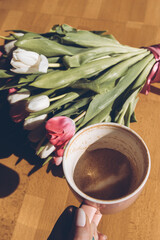 Finished cup of coffee in hand. Happy Mother's Day. Cup of coffee in hand and a bouquet of white and red tulips on the table.