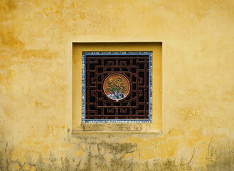 An old yellow wall with a chinese sytle window in the middle