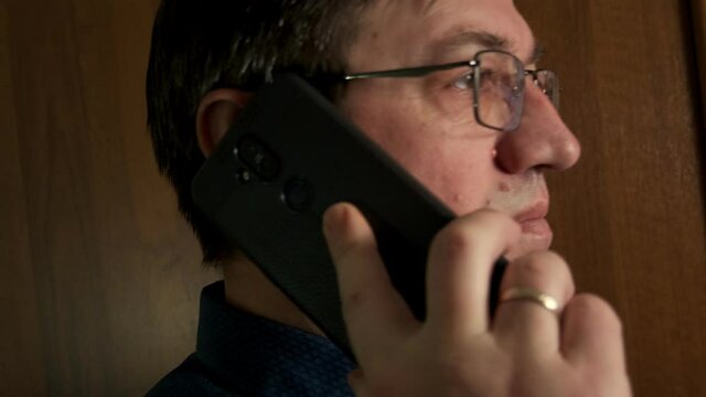 a middle-aged man with glasses takes a call on his smartphone and puts it to his ear