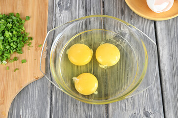 Three raw eggs are broken into a deep glass dish for making an omelet