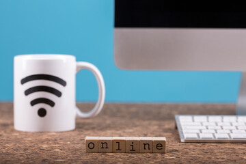 Close up view of a cork work desk interior with a computer, a mug of coffee with the sign connected,  paper, online lettering and blue background.
