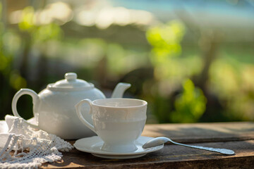 Elegant cup, lace tablecloth, teapot, wooden table. Outdoor breakfast, picnic, brunch, spring mood. Soft focus