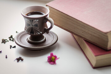 There is a beautiful coffee cup by the window. And there are books nearby