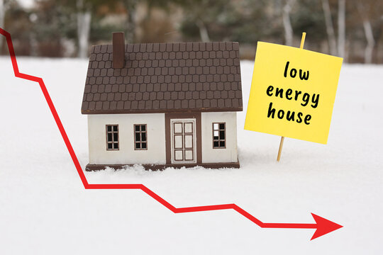 Figure of house and paper sheet with text LOW ENERGY HOUSE on snow outdoors. Concept of winter heating
