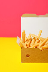Paper box with tasty french fries on color background