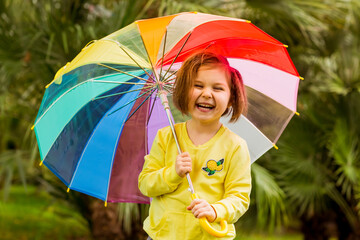 a beautiful girl in a yellow sweater and yellow boots, walking in the park with a colored umbrella