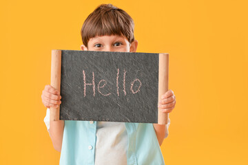 Cute little boy holding chalkboard with text HELLO on color background