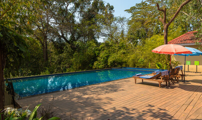 An Infinity Swimming pool with chairs with umbrella in a Indian resort.