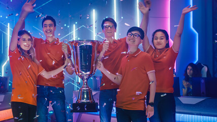Diverse Esport Team Winner of the Video Games Tournament Celebrates Victory Cheering and Holding Trophy in Big Championship Arena. Pro Computer Gaming Event with Player, Gamers, Fans Having Fun © Gorodenkoff