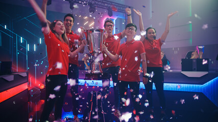Diverse Esport Team Winner of the Video Games Tournament Celebrates Victory Cheering and Holding Trophy in Big Championship Arena. Cyber Gaming Event with Gamers and Fans. © Gorodenkoff