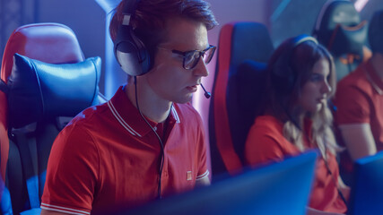 Professional Gamer Plays Computer Video Game Talking into Headset with Teammates on a Championship. Esport Team of Pro Gamers Play in Computer Game. Stylish Neon Cyber Games Arena. Portrait View © Gorodenkoff