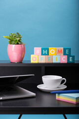 Close up view of a black work desk interior with a laptop computer, a cup of coffee,  paper, pen, plant and blue background.