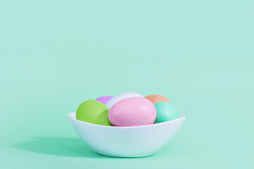 Easter background. A collection of Easter eggs in pastel colors in a plate basket on a blue-green background, with harsh shadows and light.