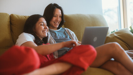 Happy Lesbian Couple Resting on the Sofa Use Laptop. Sunny Morning Two Girlfriends in Love have Fun Talking, Watching Videos, Doing e-shopping. Young Partners Share Tender Moments