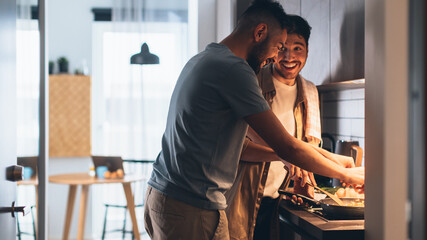 Happy Gay Couple Cooking Together in the Kitchen. Two Boyfriends in Love Spending Time Together. Boys Preparing Delicious Meal, Talk, Laugh and Have Fun. Authentically Tender Young Family Moment - Powered by Adobe