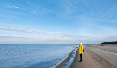 A woman in a yellow winter jacket and with a black backpack walking by the shores of the Baltic Sea near Carnikava, Latvia