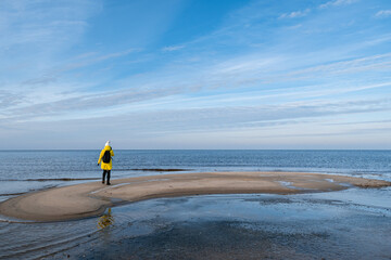 A woman in a yellow winter jacket and with a black backpack walking by the shores of the Baltic Sea near Carnikava, Latvia