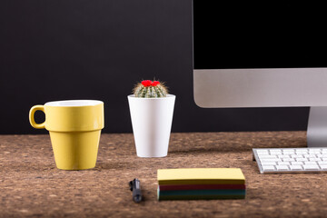 Close up view of a black work desk interior with a laptop computer, a cup of coffee,  paper, pen and, cactus with flowers black background