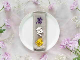 Health care, spring composition with three types of vitamins on white plate and chrysanthemums. Natural remedies that increase immunity, against viruses. Tablets, capsules, pills on floral background