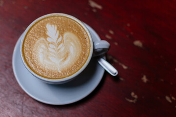 White cup with Coffee art latte on wooden table in coffee shop viewed from top. Close up. Hot latte coffee in morning, background concept, vintage color tone