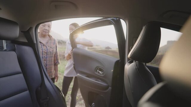 Young helpful dyed blonde daughters opening a car door for her mother to sit in, an elderly caregiver getting ready for older by fasten a back belt and close door, older people homecare concept