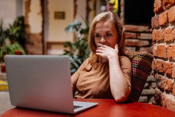 Attractive young elegant business woman spending time at cafe, working on laptop. Freelancer relaxing, thinking about new ideas. Caucasian female blogger, vintage cafe, brick wall, retro furniture