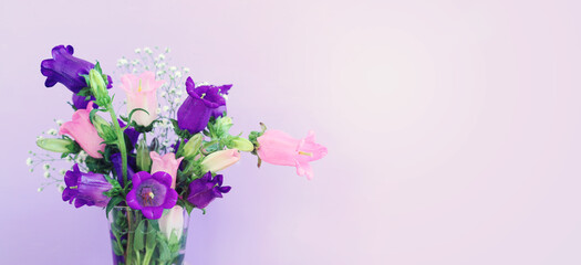 spring bouquet of purple and pink bell flowers over purple wooden background