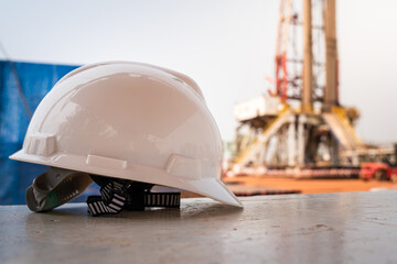 A white safety helmet in placed on table during the worker is taking a rest, with blurred background of drilling rig operation. Industrial concept background and object photo.