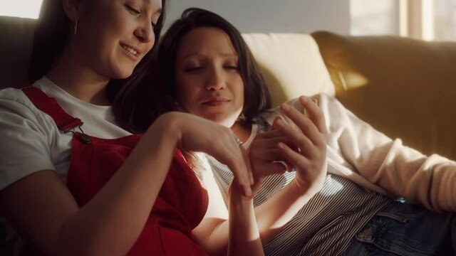 Happy Lesbian Couple Resting on the Sofa Cuddle, Touch each Other Tenderly and Sensuously. Sunny Day Two Girlfriends in Love have Fun Talking. Young Partners Share Authentically beautiful Life Moments