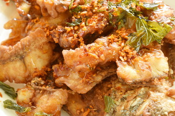 batter fried slice bass fish with chop garlic and basil leaf on plate dressing sweet sauce