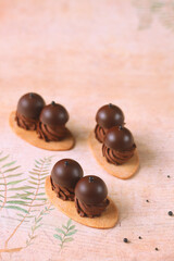 Shortcrust Oval Cookies with Chocolate Cream and Praline Bonbons on Top, on a light beige background.