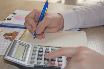 Close up man hand using calculator and writing make note with calculate about cost at home office