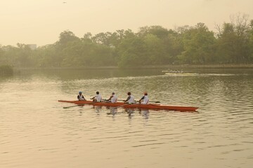 rowers rowing a long boat in the morning at rabindra sarobar lake at kolkata, west bengal, india