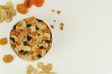 A bowl of cornflakes with dried apricots and prunes, top view. White background