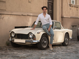 Young men posing by old classic car in town.