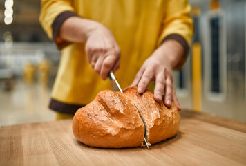 A baker at a bakery factory cuts freshly baked bread with a knife. Automated bread production.