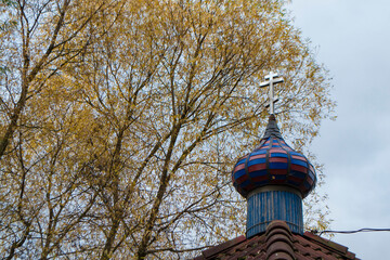 Blue and red dome of the Orthodox church in autumn time on the grey sky with yellow leaves background