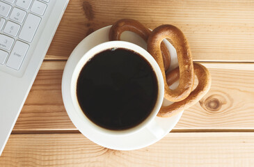 Cup with coffee drink and bagels on a wooden table next to a laptop.