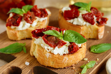 Bruschetta with sun dried tomatoes, cream cheese and basil on a wooden board.  Close up.  Italian appetazer. Selective focus