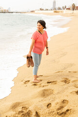 Barefoot woman on the beach with boots in hand in Barcelona, fashion concept