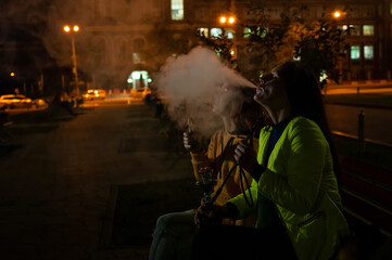 Fototapeta na wymiar Two caucasian women smoke vape and hookah outdoors at night.