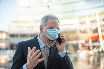 Senior masked business man yelling at the phone outdoor, covid and coronavirus concept